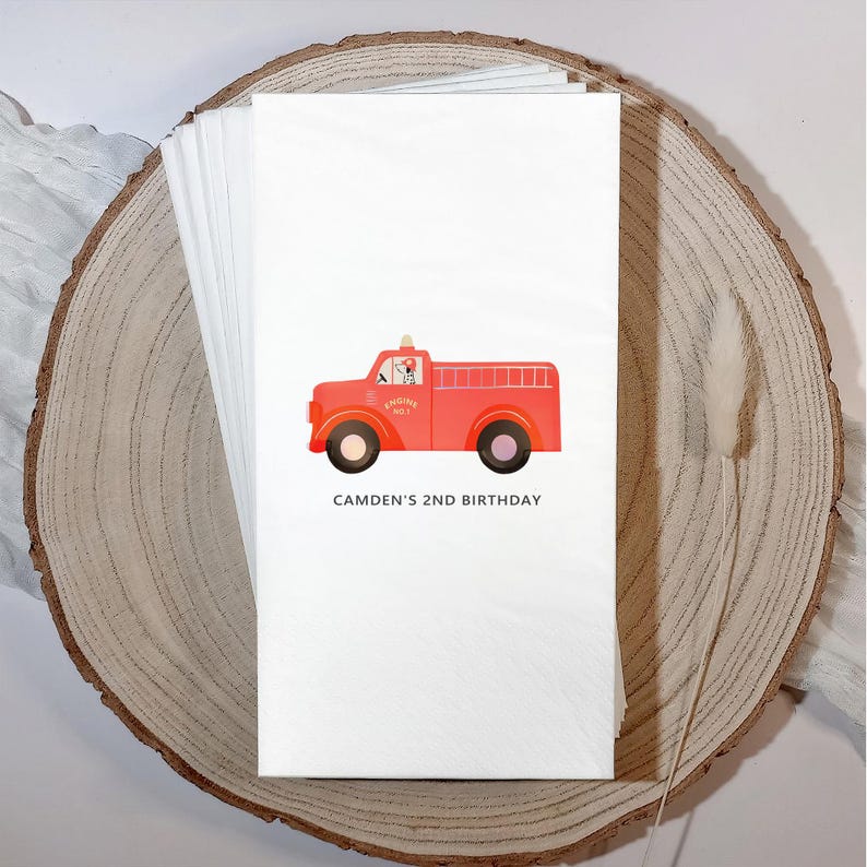 May include: White paper napkins featuring a red fire truck illustration with black wheels. The fire truck has a Dalmatian dog in the driver's seat and the text "CAMDEN'S 2ND BIRTHDAY" printed below the truck.