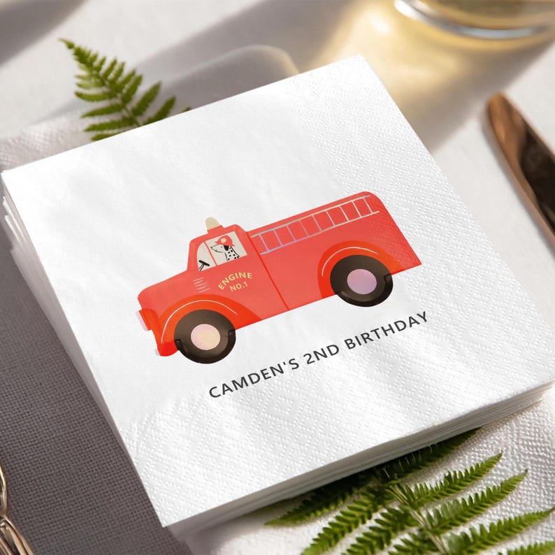 May include: White paper napkins with a red fire truck design. The fire truck has black wheels and a Dalmatian dog in the driver's seat. Text on the napkin reads "CAMDEN'S 2ND BIRTHDAY" and "ENGINE NO. 1".