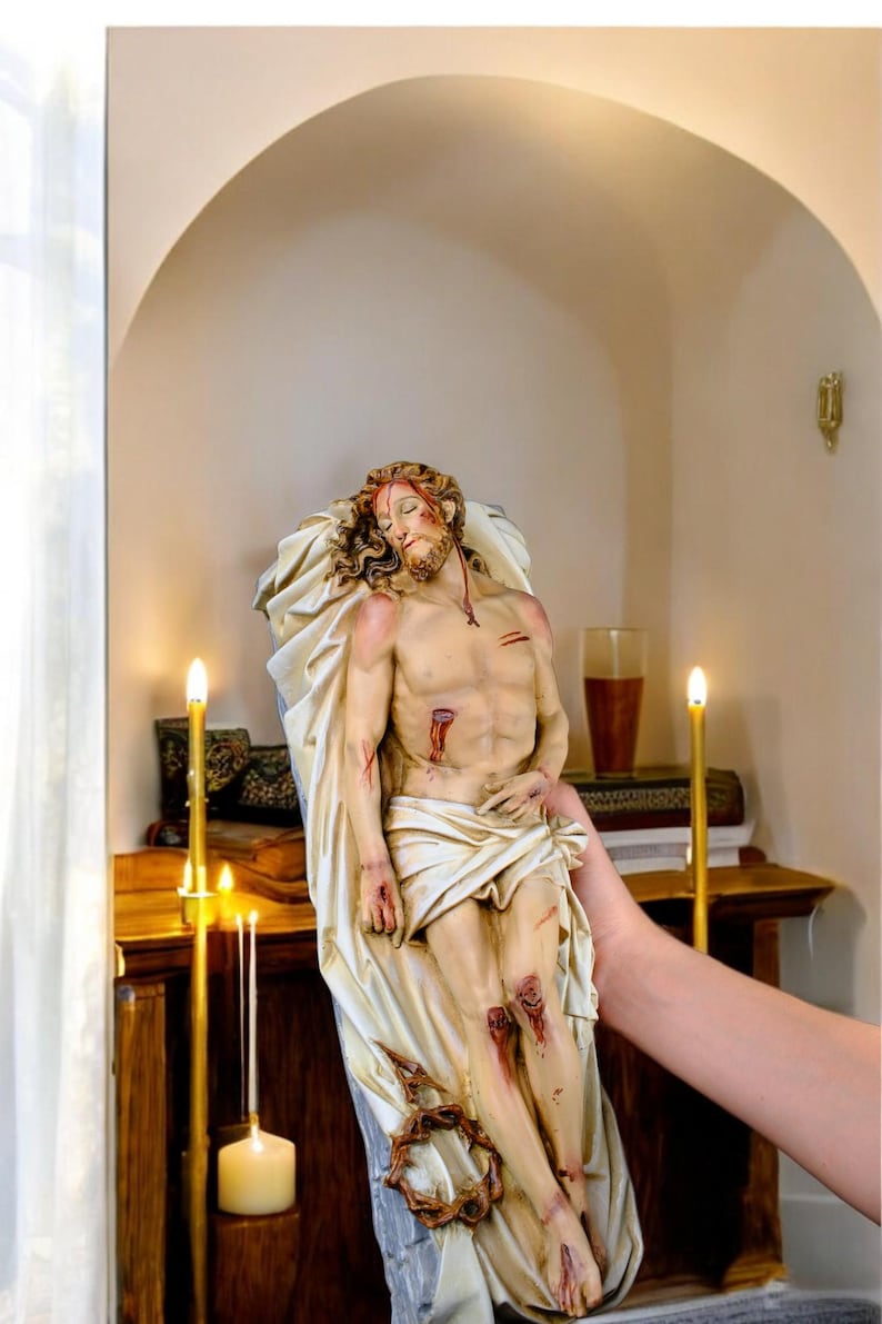 Peut inclure: Statue religieuse repr&eacute;sentant une figure bless&eacute;e, drap&eacute;e dans un tissu. La figure a une barbe et de longs cheveux, avec une couronne d'&eacute;pines &agrave; la base. La statue est tenue devant un meuble en bois avec des bougies allum&eacute;es.