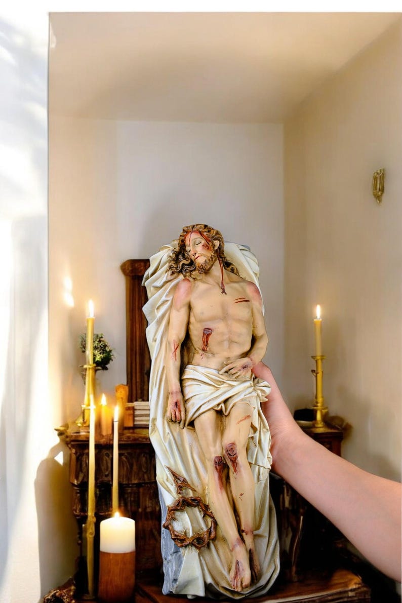 Peut inclure: Statue d&eacute;taill&eacute;e d'une figure bless&eacute;e, drap&eacute;e dans un tissu blanc. La figure a une barbe et de longs cheveux, avec une couronne d'&eacute;pines &agrave; la base. La statue est tenue devant un autel en bois avec des bougies allum&eacute;es.