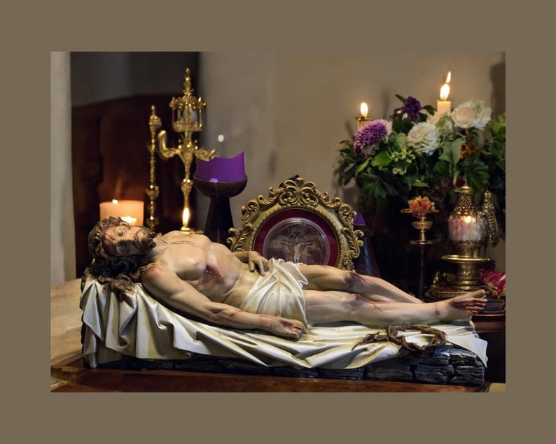 Peut inclure: Une sculpture d&eacute;taill&eacute;e d'un homme allong&eacute;, drap&eacute; dans un tissu blanc, avec une couronne d'&eacute;pines &agrave; proximit&eacute;. La sc&egrave;ne est &eacute;clair&eacute;e par des bougies et une composition florale, cr&eacute;ant une atmosph&egrave;re de recueillement. Une image encadr&eacute;e en or est en arri&egrave;re-plan.