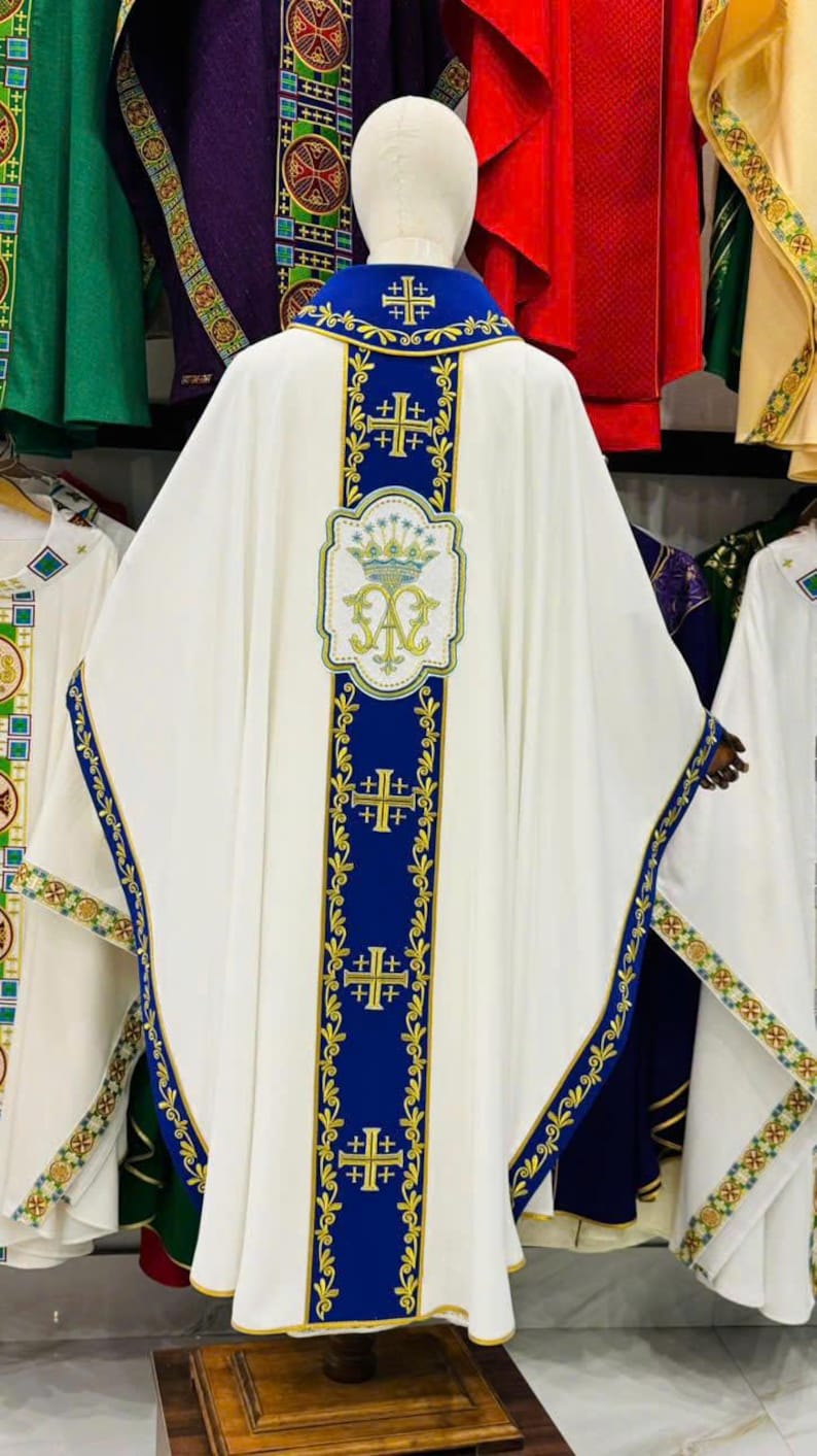 May include: White liturgical vestment with blue and gold embroidered details. The vestment features a blue collar and vertical blue panels with gold crosses. A decorative emblem is centered on the back.