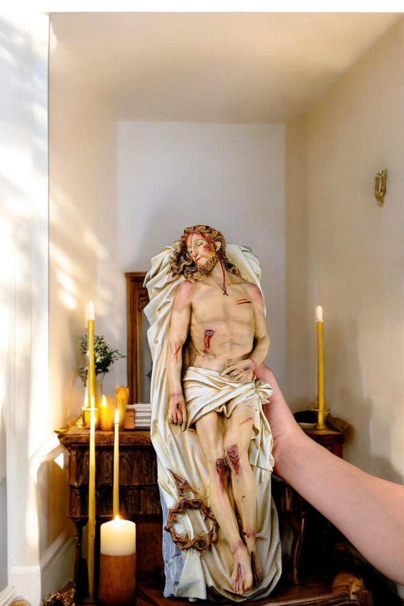 Peut inclure: Statue d&eacute;taill&eacute;e repr&eacute;sentant une figure bless&eacute;e, drap&eacute;e de tissu. La figure a une barbe et de longs cheveux, avec des blessures visibles sur le torse et les jambes. La statue est tenue devant un meuble en bois avec des bougies.