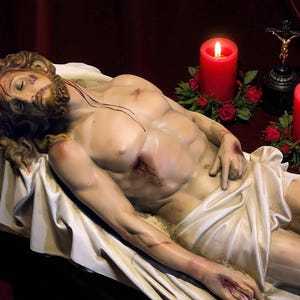 Peut inclure: Une sculpture d'un homme allong&eacute;, avec des blessures visibles sur son corps. Deux bougies rouges avec des flammes allum&eacute;es flanquent la sculpture, ainsi qu'un petit crucifix. Le fond est rouge fonc&eacute;.