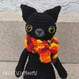 Pluszowy kotek w kolorze czarnym, wykonany szydełkiem z jesiennym szalikiem, ręcznie robiony metodą amigurumi