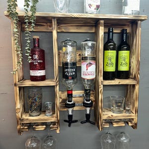 May include: A rustic, wooden bar shelf unit with multiple shelves and glass holders. It displays various bottles of liquor, wine, and gin, along with glassware. The wood has a dark, burnt finish.