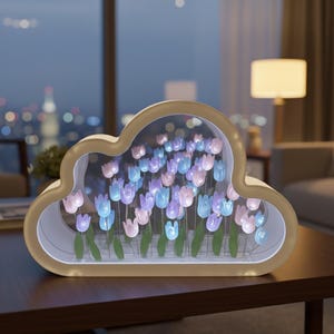 May include: A cloud-shaped decorative light fixture with a gold-colored frame. Inside, illuminated blue and pink tulip-shaped lights are arranged to resemble a flower garden. The light sits on a dark brown table.
