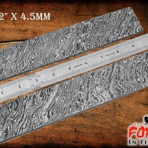 Può includere: Due pezzi di acciaio Damasco da 10 pollici per 2 pollici per 4,5 mm, un metallo a motivi utilizzato per la fabbricazione di coltelli, sono mostrati su una superficie di legno. Un righello viene utilizzato per mostrare la dimensione dell'acciaio.