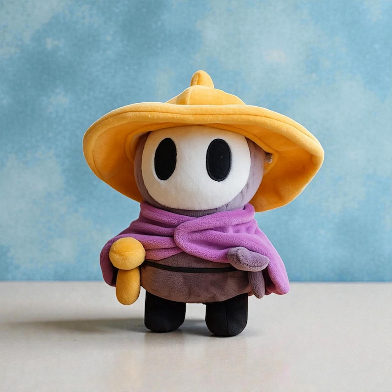 May include: A plush toy character with a large yellow hat, a white face with black oval eyes, and a purple scarf. The character has a brown body, black feet, and a small yellow mushroom-shaped accessory.