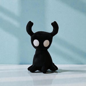 May include: A black plush toy with a horned head and large white eyes. The toy has a rounded body and a small, tentacle-like base. The background is a light blue color.