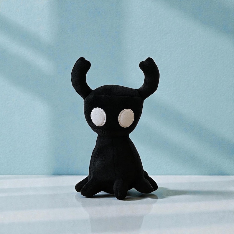 May include: A black plush toy with a horned head and large white eyes. The toy has a rounded body and a small, tentacle-like base. The background is a light blue color.