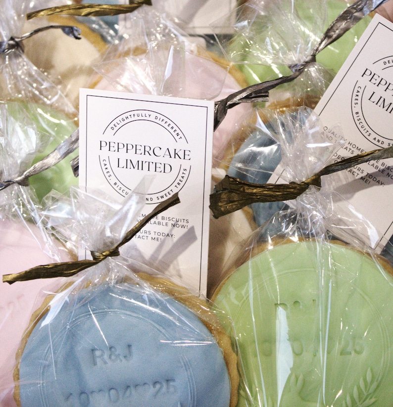 Peut inclure: Gros plan sur plusieurs biscuits emball&eacute;s individuellement dans du cellophane transparent. Chaque biscuit a un gla&ccedil;age de couleur pastel diff&eacute;rente et est nou&eacute; avec un ruban dor&eacute;. Les biscuits ont des motifs et du texte en relief. L'emballage comprend une carte "PepperCake Limited".