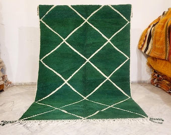 May include: A green rug with a white diamond pattern. The rug has a thick, textured pile and a fringe along the bottom edge. The rug is displayed against a white wall.