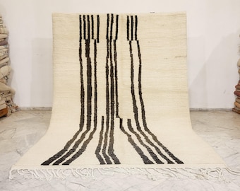 May include: Cream-colored rug with a bold, vertical black stripe design. The rug has a textured surface and a fringe along the bottom edge. This decorative rug is suitable for living rooms, bedrooms, or entryways.
