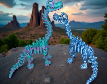 Peut inclure: Deux figurines squelettes de dinosaures. L'une est un dégradé de vert d'eau, de violet et de vert. L'autre est bleue. Elles se tiennent sur un rocher avec un paysage désertique en arrière-plan. Les dinosaures ont de longs cous et des cages thoraciques détaillées.