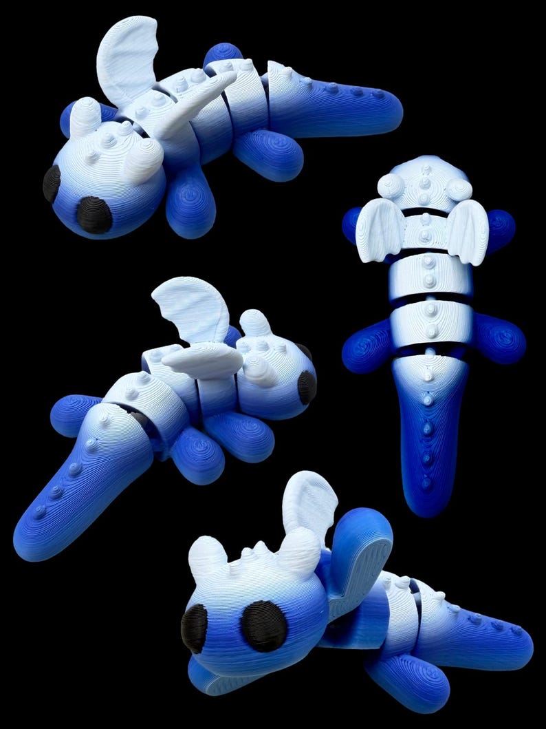 Op de afbeelding: Verschillende weergaven van een blauw en wit gearticuleerd speelgoeddraak. Het speelgoed heeft een gesegmenteerd lichaam, afgeronde ledematen en vleugelachtige structuren. De draken hebben zwarte vlekken op een zwarte achtergrond.