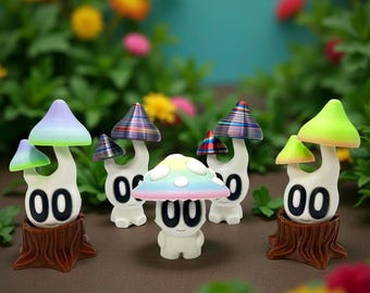Peut inclure: Plusieurs figurines de champignons fantaisistes avec des chapeaux colorés et des visages souriants. Les champignons ont une base blanche avec le numéro "00" et sont posés sur des socles en forme de souche d'arbre marron. Les chapeaux sont de couleurs variées, dont arc-en-ciel, vert et bleu.