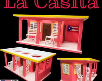 Peut inclure: Répliques miniatures de maisons roses avec des bordures jaunes et des chaises blanches. Le texte "La Casita" est affiché en haut. Le drapeau portoricain est visible sur l'une des maisons. La phrase "Made in the USA" est affichée avec le drapeau américain.