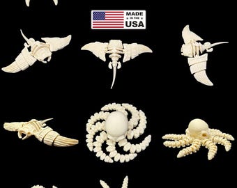 Peut inclure: Collection de sculptures de créatures marines sculptées en blanc cassé, comprenant des crabes, des raies et des céphalopodes, sur fond noir. L'image comprend une étiquette "Made in the USA".