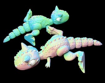 Peut inclure: Deux figurines de dinosaures colorées dans des tons de vert, de bleu et de rose sont présentées sur un fond noir. Les dinosaures de dessins animés ont de grands yeux, des têtes pointues et des corps texturés, ce qui leur donne un aspect ludique.