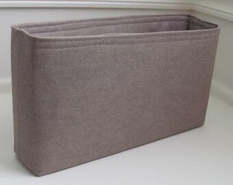 May include: A beige fabric organizer insert for a handbag. The insert is rectangular and has a smooth, textured surface.