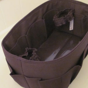 May include: A brown fabric organizer with multiple compartments and a single elastic band. The organizer is designed to fit inside a larger bag.