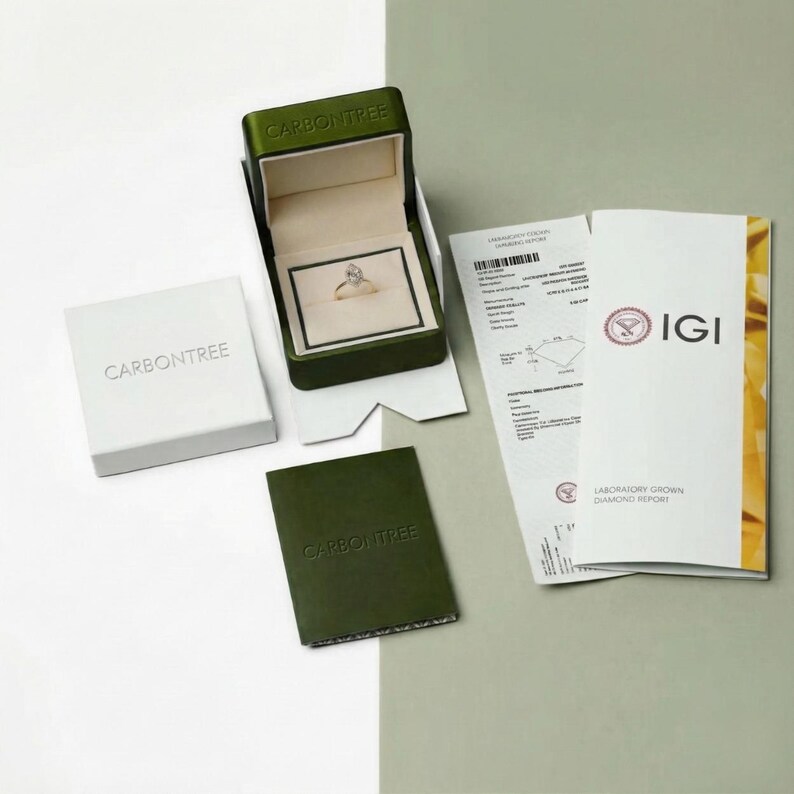 Pu&ograve; includere: Un anello con diamante taglio marquise &egrave; posizionato all'interno di un cofanetto in velluto verde scuro aperto con la scritta CARBONTREE. Accanto si trovano un coperchio bianco, un cartoncino verde scuro con CARBONTREE e un certificato IGI.