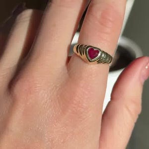 Pu&ograve; includere: Un anello in oro con una pietra preziosa rossa centrale a forma di cuore. La fascia presenta un design a coste testurizzato che si assottiglia verso il retro. Il metallo ha una finitura lucida e la pietra rossa &egrave; incastonata nel cuore.
