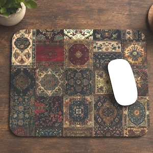 May include: A rectangular mousepad with a patchwork design of ornate, vintage rug patterns in shades of red, blue, and gold. A white computer mouse rests on the pad, next to a laptop, a notepad, and a coffee cup.