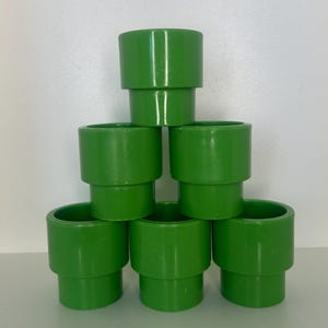 May include: A pyramid of six bright green plastic pipe pieces. Each piece is cylindrical with a wider top and bottom, connected by a narrower section. The pipes are stacked against a white background.