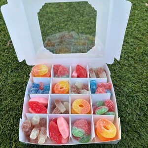 May include: A white box with a clear window filled with assorted gummy candies in various colors and shapes. The candies are arranged in a grid pattern.