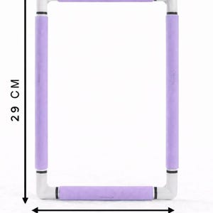 Peut inclure: Un cadre à broder rectangulaire composé de tubes en plastique blanc avec des poignées en mousse lavande sur chaque côté. Le cadre mesure 29 cm de hauteur et 21 cm de largeur, comme indiqué par les flèches et les étiquettes de dimension noires.