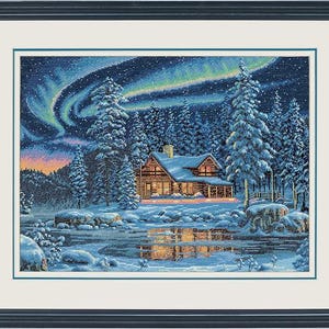 May include: A framed cross-stitch embroidery depicting a log cabin in a snowy forest at night. The scene features a vibrant green and blue aurora borealis in the sky, snow-covered pine trees, and a glowing cabin reflected in a frozen pond.