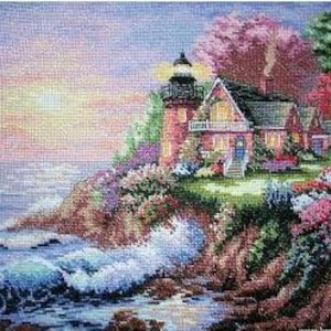 Puede incluir: Una imagen de punto de cruz de una escena costera con un faro rojo y una casa con techo gris. La escena incluye olas rompiendo, flores coloridas y una puesta de sol. El faro tiene una parte superior negra.