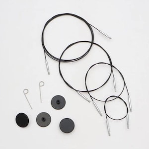 Könnte beinhalten: Ein Set bestehend aus drei schwarzen runden Endkappen, zwei kleinen Metallstiften zum Festziehen und drei flexiblen schwarzen Rundkabeln mit silberfarbenen Metallanschlüssen an beiden Enden für austauschbare Stricknadelsysteme.