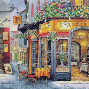 Puede incluir: Un bordado de punto de cruz que representa una escena callejera con un restaurante llamado L'Antico Sigillo. La imagen muestra un escaparate amarillo, mesas al aire libre con manteles naranjas, una bicicleta y arreglos florales en punto de cruz.