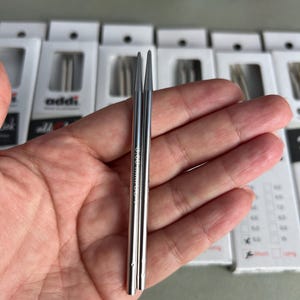 Pode incluir: Duas pontas de agulha de tricô de metal na cor prata com extremidades pontiagudas. As agulhas estão marcadas com o texto 3.50 mm / US 4. As agulhas estão posicionadas verticalmente e paralelas entre si, com um acabamento liso e reflexivo.