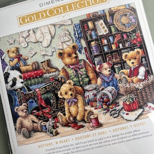 Puede incluir: Un kit de punto de cruz contado Dimensions Gold Collection titulado Buttons 'N Bears. El empaque presenta una ilustración de varios osos de peluche en un cuarto de costura con carretes de hilo, una máquina de coser y botones.