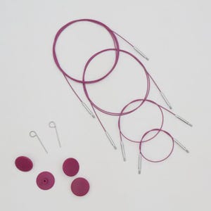 Könnte beinhalten: Ein Set aus drei flexiblen magentafarbenen Stricknadelkabeln mit silbernen Metallanschlüssen an beiden Enden. Das Set enthält zwei kleine silberne Metallschlüssel zum Festziehen und vier runde magentafarbene Endkappen zur Maschensicherung.