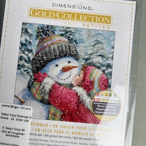 以下が含まれることがあります： Dimensions Gold Collection Petitesのクロスステッチキット「A Kiss for Snowman」。雪だるまと冬服を着た子供のイラストが描かれています。透明なプラスチックパッケージには、糸オーガナイザーと18カウントの白いアイーダ布が含まれています。