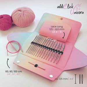 Może przedstawiać: Różowy i wielokolorowy zestaw drutów do robienia na drutach z napisem "addi Click Unicorn" i "Lace Long 3,5 - 8,0 mm US 4-11". Zestaw zawiera druty, różowy kabel i dwie kulki przędzy. Etui ma około 12,5 cm.