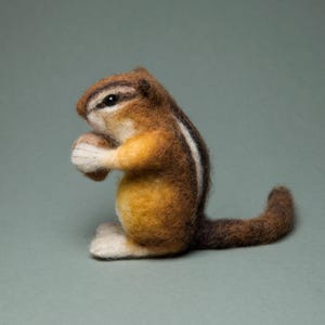 Könnte beinhalten: Ein braunes und weißes Nadelfilz-Eichhörnchen, das eine Nuss in seinen Pfoten hält. Das Eichhörnchen hat einen langen, buschigen Schwanz.