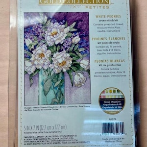 May include: A Dimensions Gold Collection Petites White Peonies cross stitch kit in clear plastic packaging. The kit includes presorted thread, 18 count white Aida, a needle, and instructions. The finished size is 12.7 cm by 17.7 cm.