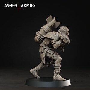 Pode incluir: Uma miniatura cinza de uma figura curvada carregando uma bomba grande nas costas, presa com corda. A figura veste roupas esfarrapadas com s&iacute;mbolos de cruz e bandagens nas pernas. O texto ASHEN ARMIES &eacute; vis&iacute;vel no canto superior esquerdo.