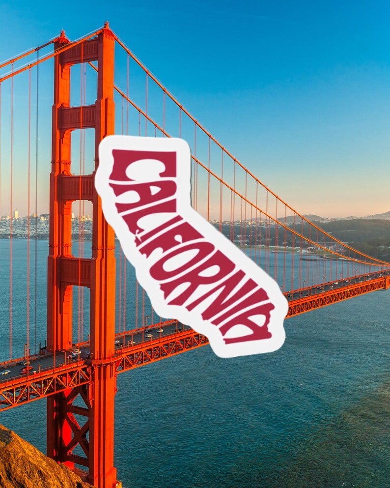 May include: A sticker in the shape of California with the word "CALIFORNIA" in red, overlaid on a photo of the Golden Gate Bridge. The bridge is a vibrant orange, spanning across blue water under a clear sky.