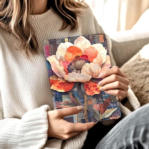 May include: A floral journal featuring a large, detailed flower in shades of orange, pink, and cream. The flower is set against a patchwork background of blues, greens, and browns. The journal is held in a person's hands.