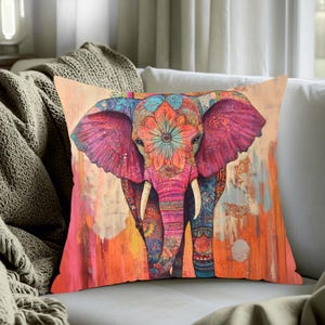 May include: A decorative square pillow featuring a colorful, artistic elephant design. The elephant is depicted with intricate patterns in shades of pink, orange, blue, and purple. The pillow is on a white couch.