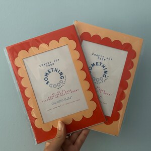 May include: Two rectangular picture frames with scalloped edges. One frame is red with a peach-colored interior, and the other is peach with a red interior. Each frame has the text "Crafty Joy From Something Good Workshop" and "A4 to A5 Scalloped Edge Picture or Photo Mount."