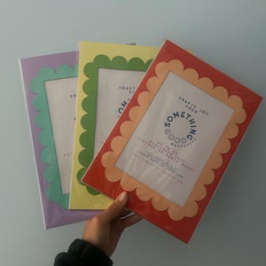 May include: Three picture frames with scalloped edges in purple, yellow, and red. The frames have a white interior with text that reads "Crafty Joy from Something Good Workshop". The frames are held against a light blue background.