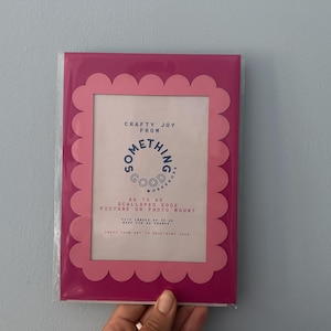 May include: A pink scalloped edge picture or photo mount with the text "Crafty Joy From Something Good Workshop". The frame is in a clear plastic sleeve. The frame fits 5x7 inch photos.